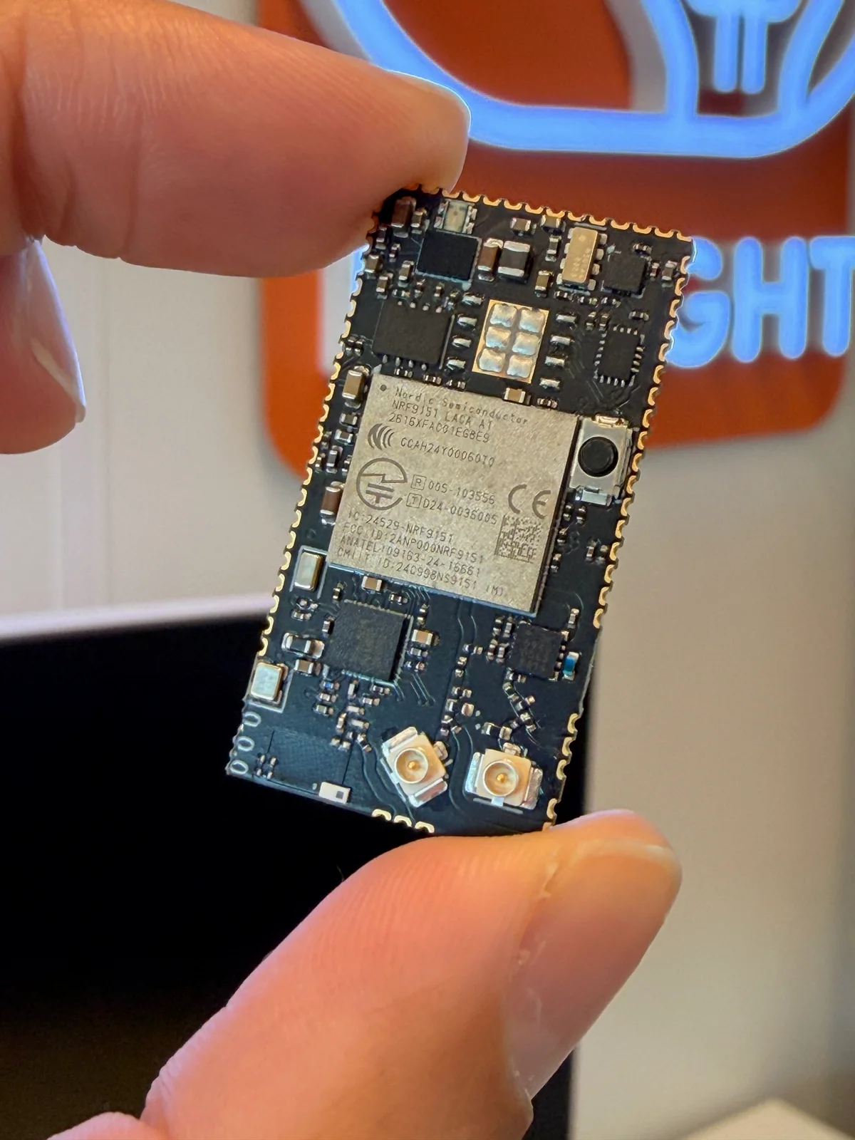 Top side of the actual CAS Module with nRF9151, components and u.FL connectors, held between two fingers